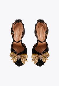 Czarne aksamitne szpilki z dodatkiem sztucznej kokardy ozdobionej złotymi elementami. Regulowany pasek z złotą klamrą. Pikowana wkładka.