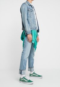 Ljusblå denimjacka, vit skjorta, grön sweatshirt knuten runt midjan, ljusblå uppvikta jeans och gröna sneakers med vita detaljer.