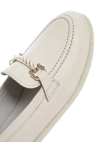 Mocassini in pelle beige con un dettaglio decorativo a catena dorata sulla parte superiore, con punta rotonda e suola in gomma testurizzata.