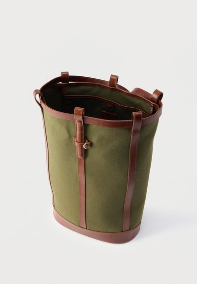 Πράσινη υφασμάτινη τσάντα tote με καφέ δερμάτινα λουριά, περιθώριο και λεπτομέρεια αγκράφας, εμφανιζόμενη ανοιχτή σε λευκό φόντο.