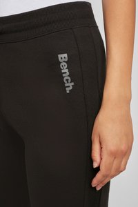 Schwarze Jogginghosen mit geripptem Bund; verfügt über ein graues "Bench"-Logo an der Seite; glatte Textur mit enganliegendem Schnitt.