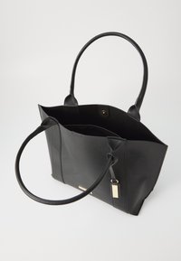 Sac fourre-tout noir en cuir lisse avec deux longues poignées, un haut ouvert et un détail en métal doré sur le côté.