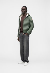 Vihreä untuvatakki hupulla, kevyt malli, jossa on beige vuori. Yhdistetty harmaisiin farkkuihin ja valkoisiin lenkkareihin.