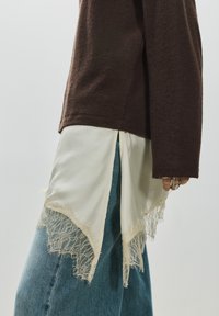 Barna texturált felső, krémszínű szatén darab rétegezve csipkés szegéllyel. Látható világoskék színű, bő szabású farmernadrág.