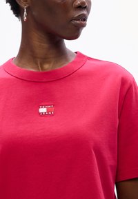 Lyserød bomulds T-shirt med rund halsudskæring og et lille broderet logo patch med "TOMMY JEANS" på forsiden. Korte ærmer.