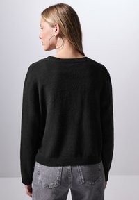 Svart stickad tröja med texturerad yta, bred rund halsringning och ribbad fåll. Tillsammans med ljusgrå högmidjade jeans och stora hoopörhängen.