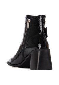 Botines de charol negro con punta afilada, cierre lateral con cremallera y un tacón grueso y texturizado. La superficie tiene un acabado brillante.