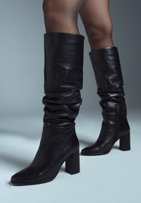 Zwarte leren kniehoge laarzen met een slouchy ontwerp, vierkante neus en chunky hak. Voorzien van een zijrits en een gladde textuur.