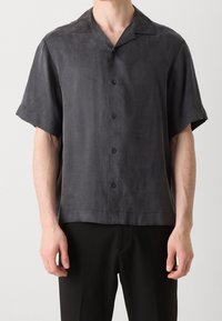 Camisa de manga corta en tela gris oscuro con una textura sutil, que cuenta con un cuello estándar, cierre de botones en la parte delantera y botones negros.