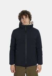 Giacca imbottita blu con cappuccio, dotata di chiusura con zip, tasche laterali e un rivestimento di colore chiaro a contrasto. Texture liscia e design moderno.