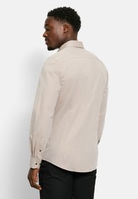 Hellbeiges, langärmliges Hemd mit strukturiertem Kragen, knöpfbaren Manschetten und dezent texturiertem Stoff. Taillierte Passform mit geradem Rücken.