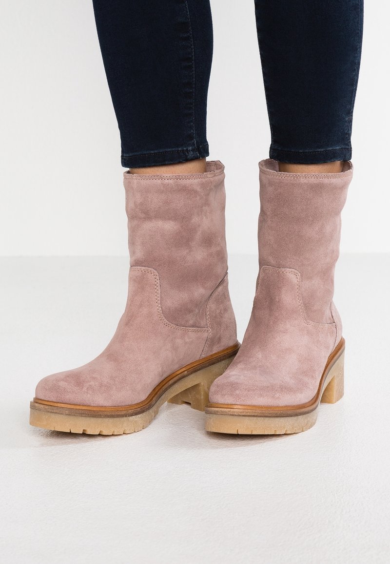 Suede ankle boots in soft pink with a chunky wooden heel and textured rubber sole. The design features clean lines and minimal stitching.