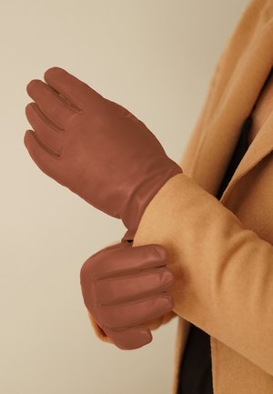 Braune, strukturierte Lederhandschuhe mit gerippten Details, die ein figurbetontes Design zeigen. Auf einer Hand vor einem neutralen Hintergrund präsentiert.