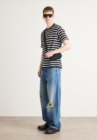 Black and white striped T-shirt, blue distressed jeans, black crossbody bag, black sunglasses, and chunky black shoes on a neutral background.