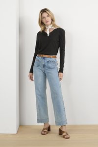 Fekete, hosszú ujjú póló V-nyakkal, világoskék, bő szárú farmernadrág csipkés szegéllyel, és barna magassarkú szandál. Selyem sál kötve a nyaknál.