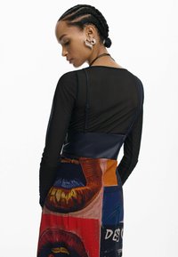 Top nero a maniche lunghe in materiale trasparente; gonna colorata con motivo grafico di labbra; presenta orecchino a forma di cuore argentato e spalline sul retro.