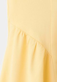 Tissu jaune avec une couture diagonale et des plis froncés créant une texture sur le matériau du vêtement.