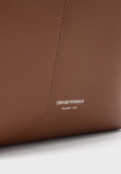 Кафява кожена повърхност с текстура, с видими шевове и бяло лого Emporio Armani Milano 1981, отпечатано близо до долния ръб.