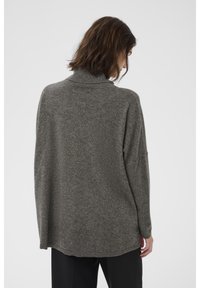 Pelēks adīts džemperis ar augstu kaklu, brīvu piegriezumu, nolaižamām plecu līnijām un ribota apdare kaklā un apakšgalā. Mīksta, strukturēta auduma.