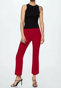 Zwarte geribbelde tanktop gecombineerd met strakke rode broeken met een flared model, zachte textuur en zwarte sandaaltjes met bandjes.