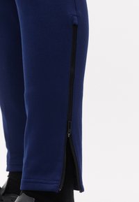 Κοντινό πλάνο σκούρων μπλε παντελονιών με μερικώς ανοιχτό μαύρο πλευρικό φερμουάρ κοντά στον αστράγαλο, φορεμένα πάνω από μαύρες κάλτσες και παπούτσια.