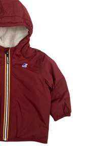 Giacca rossa per bambini con cappuccio, foderata in pile bianco, con polsini elastici e zip anteriore caratterizzata da strisce gialle e rosse.