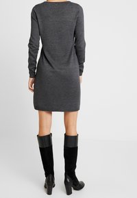 Robe en tricot grise à manches longues avec une coupe droite, des ourlets côtelés et un col rond, associée à des bottes noires à talons montantes.