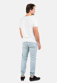 Camiseta blanca de manga corta, pantalones jogger azul claro con puños elásticos y zapatillas negras. Diseño simple, corte casual, sin patrones visibles.