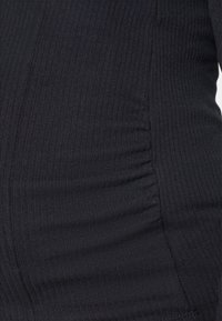 Schwarzer gerippter Stoff mit subtiler Textur und leichten Raffungselementen an der Seite. Das weiche Stretchmaterial verbessert die Passform und den Komfort.