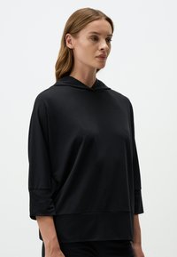 Felpa nera con cappuccio, dalla vestibilità morbida, maniche a tre quarti e texture liscia. Presenta un design minimalista senza loghi o motivi visibili.