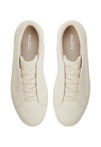 Beżowe buty slip-on z teksturowanej powierzchni, posiadające elastyczne sznurówki i wytłoczone logo na języku. Gumowa podeszwa zapewniająca przyczepność.