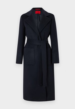 Długi czarny wełniany płaszcz z szerokimi klapami, paskiem do wiązania w talii, dwoma przednimi naszywanymi kieszeniami oraz czerwoną metką wewnątrz.