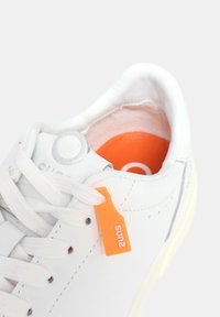 Sneaker bianca con pelle liscia, punta rotonda e soletta arancione. Include lacci bianchi e un'etichetta arancione con il testo "suna".