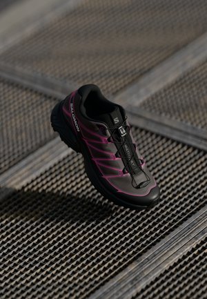 Salomon black and pink running shoe features a mesh upper, molded sole, and a quick-lacing system for secure fit. Textured surface detail visible.