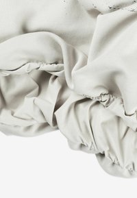 Miękka szara bawełniana tkanina ze ściągaczem na elastycznym brzegu, ukazująca fałdy i zagniecenia, co wskazuje na teksturowany, drapowany wzór.