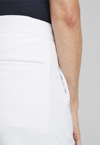 Pantalones blancos con una textura suave y un brillo sutil. Diseñados con un bolsillo trasero y una cinturilla elegante.