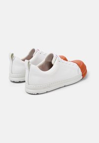 White leather sneakers with a rounded orange rubber toe cap, textured back, and white laces. Subtle green accent on the heel pull tab.