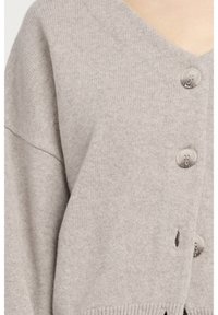 Ljusgrå stickad kofta med V-hals, stora knappar och sidofickor, i en mjuk textur och lös passform.