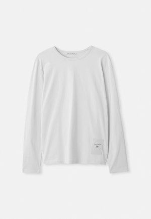 White long-sleeve T-shirt made of soft cotton. Features a round neckline and a small branded tag on the lower left side.
