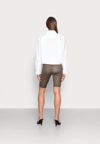 White shirt with long sleeves paired with brown patterned bike shorts. Model wears black high-heeled shoes, showing smooth texture and fitted design.