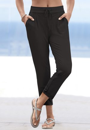Pantaloni jogger leggeri neri con vita regolabile tramite cordoncino, tasche laterali e design a gamba affusolata. Indossati con ciabatte con dettagli argentati.