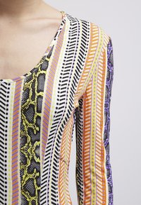 Långärmad topp med flerfärgade ränder i orange, lila och svart med ett ormskinnsmönster och rundad halsringning.