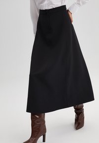 Black, knee-length A-line skirt with a fitted waist, single button closure, and smooth fabric texture. Worn with brown leather knee-high boots.