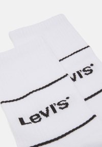 Baltas kokvilnas zeķes ar ribotu tekstūru, melnām horizontālām svītrām un izteiksmīgu melnu "Levi's®" logotipu.