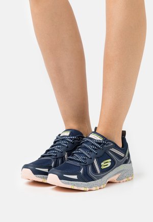 Námořnické modré sportovní boty s síťovaným svrškem, reflexními akcenty a růžovou gumovou podrážkou. Mají složitý design tkaniček a kontrastní šedé detaily.