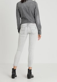 Pantalones vaqueros de mezclilla gris con un ajuste ajustado, que cuentan con un diseño clásico de cinco bolsillos y una sutil costura en los bolsillos traseros, combinados con botines al tobillo.