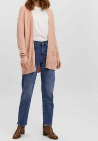 Ljusrosa ribbad cardigan med långa ärmar och två framfickor, kombinerad med en vit t-shirt och blå högmidjade jeans. Bruna ankelstövlar.