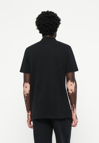 Fekete pamut póló kerek nyakkal és rövid ujjakkal, laza fazonnal és sima textúrával. A hátulnézeti képen a dizájn részletei láthatók.