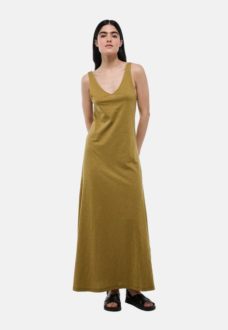 Robe maxi vert olive avec de larges bretelles, décolleté en V et coupe décontractée, associée à des sandales plates noires. Texture de tissu lisse.