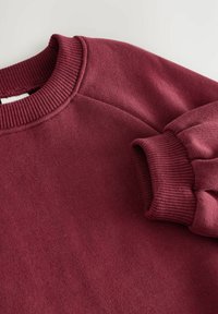 Bordeauxfarbener Sweatshirt mit geripptem Rundhalsausschnitt und Bündchen, das eine weiche Textur und einen lässigen Schnitt aufweist. Nahtdetails an den Schultern.